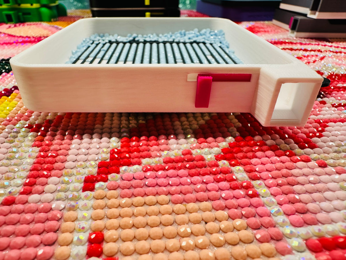 Side view of a white diamond art tray showing its built-in hot-pink sliding spout latch and rectangular pouring spout, with light-blue drills inside.