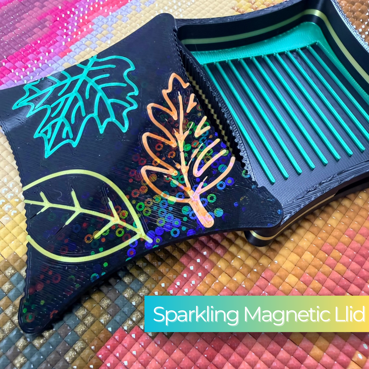 A small ergonomic magnetic diamond art tray from the Autumn Series,  embroidered leaf designs on lid magnetic base on a black tray with green lines. sparkling lid