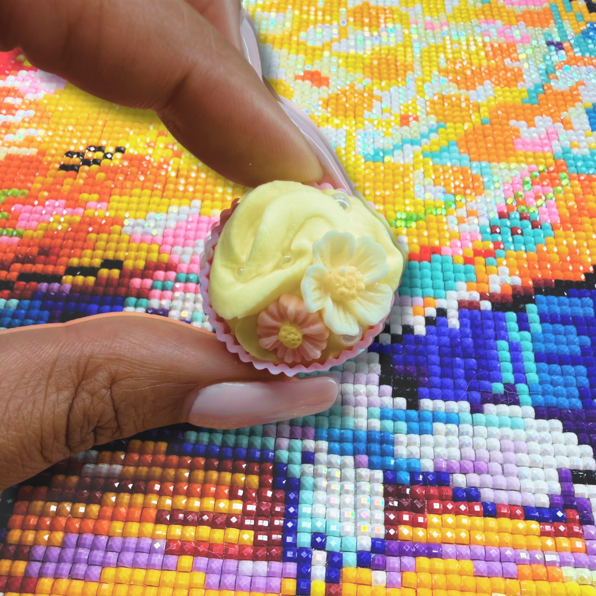 Small decorative cupcake held by a hand on a colorful cross-stitch background