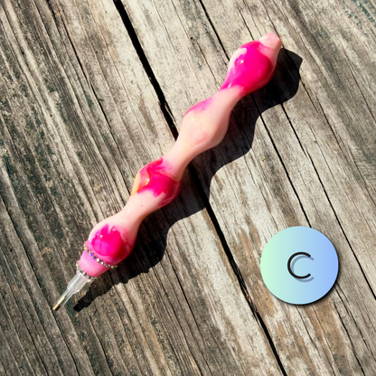 A pink and white marbled silicone personal massager with a clear suction tip, displayed diagonally on a weathered wooden plank surface next to a circular blue and green gradient scale marker.